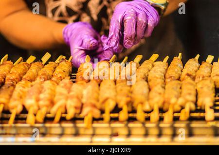 Nahaufnahme des Verkäufers, der Schweinesatay gegrillt, Thai-Steak, gebratenes Schweinefleisch, das auf dem Feuerbildschirm auf dem Nachtmarkt in Bangkok, Thailan, gegrillt wird Stockfoto