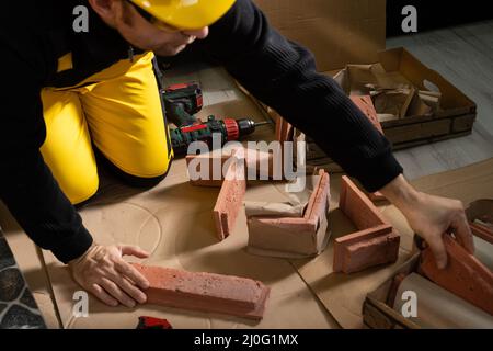 Der Bauarbeiter greift nach einer weiteren gemauerten Zierfliese, um die geplanten Arbeiten fortzusetzen. Bauarbeiter Stockfoto