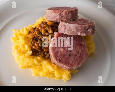 Cotechino, eine große italienische Schweinswurst mit Linsen und Polenta, ein traditionelles Silvesterdinnern in Italien Stockfoto