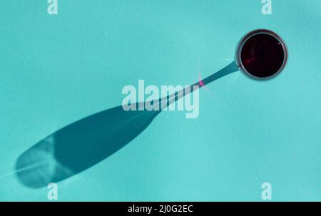 Weinglas von Rotwein mit einem Schatten auf einem aquamarinfarbenen Hintergrund Draufsicht flach Lay Stockfoto