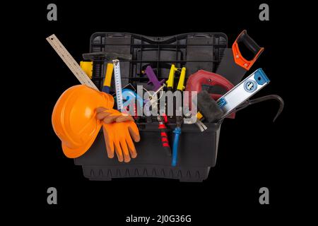 Eine offene schwarze Kunststoff-Werkzeugkiste mit einem orangefarbenen Schutzhelm und verschiedenen Handwerkzeugen, die auf einem schwarzen Hintergrund isoliert sind, schließen sich Stockfoto