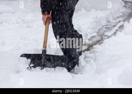 Ein Mann reinigt Winterwege im Hof mit einer Schaufel vom Schnee im Schneefall Stockfoto