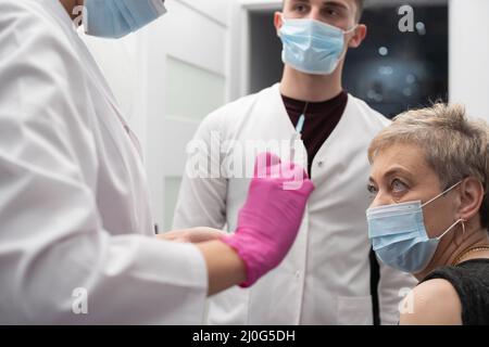 Vor der Injektion überprüft die Krankenschwester den Inhalt der Spritze. Eine Frau in ihren 50s Jahren wartet auf einen Impfstoff von COVID19 Jahren. Stockfoto