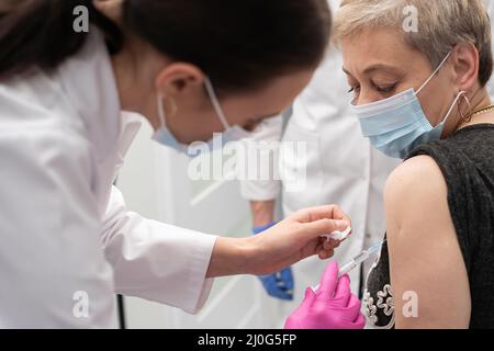 Eine Krankenschwester macht einen Impfstoff gegen eine ältere Frau. Der COVID vaccine19. Eine sterile Arztpraxis in einer Privatklinik. Ein junges Ich Stockfoto