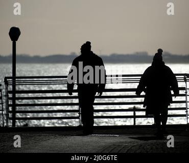 Menschen in Silhoutte mit Blick über den Zaun am Meer. Stockfoto