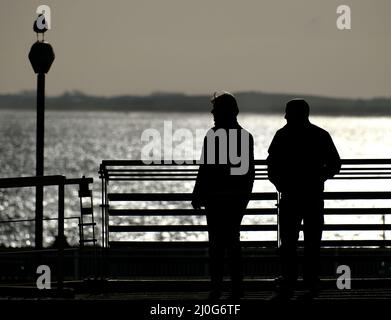 Menschen in Silhoutte mit Blick über den Zaun am Meer. Stockfoto