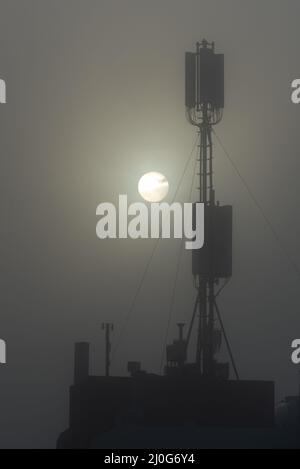 Kommunikationsturm auf einem Gebäude mit 4G 5G Antenne bei Sonnenaufgang im Nebel. Stockfoto