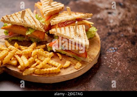 Club Sandwiches auf einem Holzbrett serviert. Mit heißen Pommes frites Stockfoto