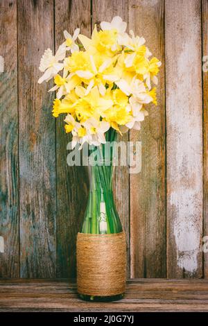 Blumenstrauß aus Narzissen in selbstgemachter Vase auf Holzhintergrund Stockfoto