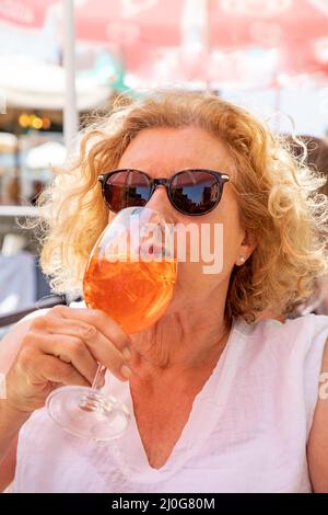 Attraktive Frau trinkt ein rot gefärbtes Getränk wie Aperol Spritz, Erdbeersaft, Orangensaft mit Eis Stockfoto