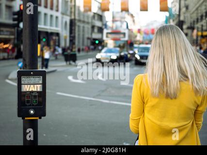 Nicht erkannte Person, die an einer Kreuzung wartet. Wartenschild leuchtet auf. Stockfoto
