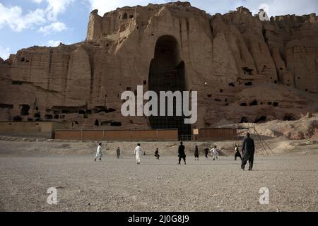 Bamiyan. 18. März 2022. Das am 18. März 2022 aufgenommene Foto zeigt Menschen, die in der Nähe der Bamiyan Buddha Statue in der Provinz Bamiyan, Zentralafghanistan, Fußball spielen. Quelle: Saifurahman Safi/Xinhua/Alamy Live News Stockfoto