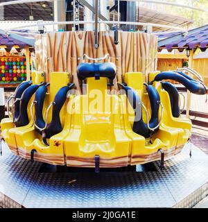 Gelbe Attraktion mit leeren Sitzen, die in einem Kreis angeordnet sind. Vergnügungspark Stockfoto