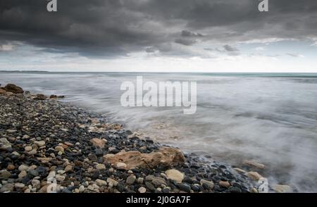 Seeschiffe planschen mit Steinen an die Küste gegen den stürmischen dramatischen Wolkenhimmel. Winterzeit, Limassol zypern Stockfoto