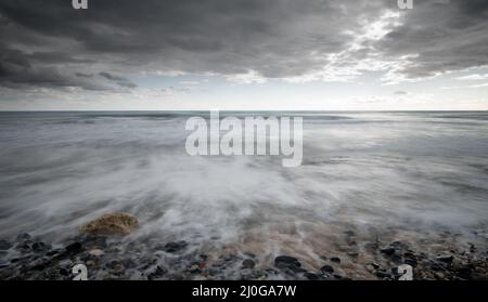 Seeschiffe planschen mit Steinen an die Küste gegen den stürmischen dramatischen Wolkenhimmel. Winterzeit, Limassol zypern Stockfoto