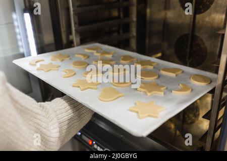 Der Konditor setzt Cookies verschiedener Formen in den Ofen Stockfoto