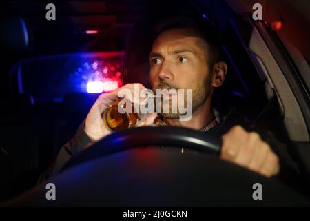 Die Polizei stoppte das Auto mit betrunkenem Fahrer im Inneren. Betrunkener Mann, der während des Autofahrens Alkohol trinkt. Fahrer unter Alkoholeinfluss Stockfoto