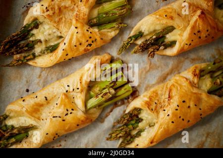 Gebackener grüner Spargel in Blätterteig, mit Sesamsamen bestreut. Auf ein weißes Backpapier gelegt Stockfoto