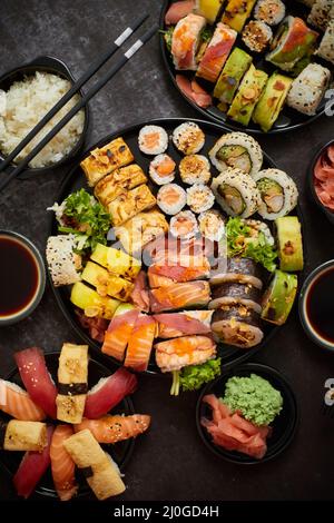 Verschiedene Sushi-Gerichte auf dunklem Hintergrund. Blick von oben auf Meeresfrüchte, verschiedene Maki-Brötchen Stockfoto