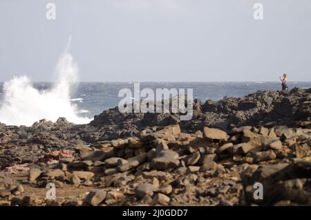 El Confital, 27. Februar 2022: Frau fotografiert eine Welle, die bricht. Las Palmas de Gran Canaria. Gran Canaria. Kanarische Inseln. Spanien. Stockfoto