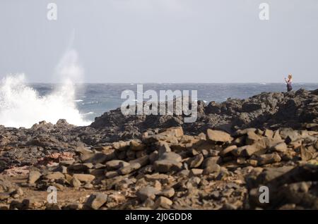 El Confital, 27. Februar 2022: Frau fotografiert eine Welle, die bricht. Las Palmas de Gran Canaria. Gran Canaria. Kanarische Inseln. Spanien. Stockfoto