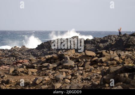 El Confital, 27. Februar 2022: Frau fotografiert eine Welle, die bricht. Las Palmas de Gran Canaria. Gran Canaria. Kanarische Inseln. Spanien. Stockfoto