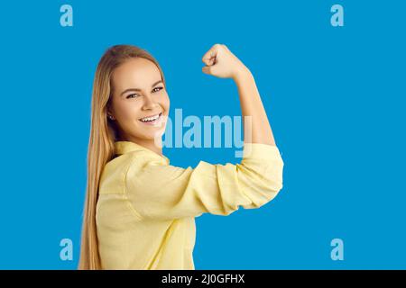 Glückliche selbstbewusste junge Frau lächelt und beugte ihren Arm isoliert auf blauem Hintergrund Stockfoto