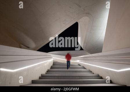 Unbekannte Person, die an der Treppe zu einem hellen offenen Raum geht. Stockfoto