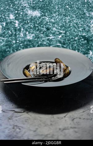 Schwarze Spaghetti mit Meeresfrüchten und Venusmuscheln auf schwarzem Teller Auf dunklem Stein Stockfoto