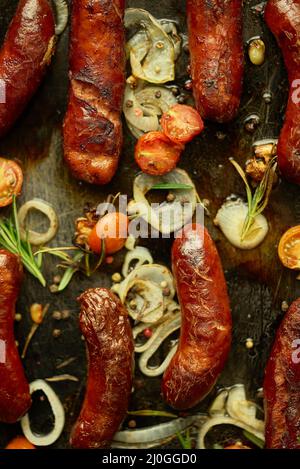 Leckere gegrillte hausgemachte Rosmarinwürste auf einem eisernen Bratblech Über rustikalem Tisch aus dunklem Stein Stockfoto