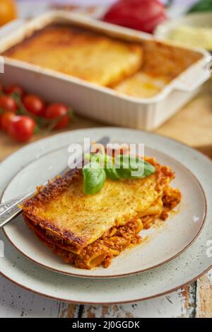 Hausgemachte leckere Fleischlasagne mit frischem Basilikum und Parmesankäse In einem Teller auf Holzgrund Stockfoto