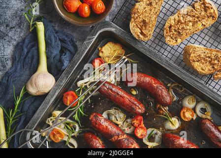 Leckere gegrillte hausgemachte Rosmarinwürste auf einem eisernen Bratblech Über rustikalem Tisch aus dunklem Stein Stockfoto