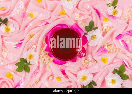 Eine Tasse Tee auf einem Hintergrund aus rosa Stoff in rosa Rosenblüten Stockfoto