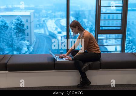 Eine junge Frau, die in einem modernen Raum sitzt, während sie an einem Projekt auf einem Laptop arbeitet. Selektiver Fokus Stockfoto