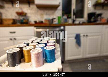 Organisierte Vielfalt an farbigen Nähfäden in einer Tragetasche mit einer weißen Küche im Hintergrund Stockfoto