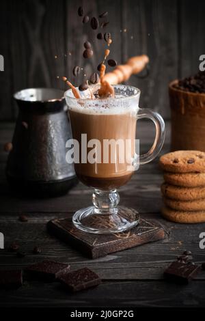 Kaffee mit Creme mit Spritzern und Körnern im Flug mit Keksen auf dunklem Holzhintergrund Stockfoto