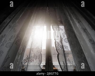 Sonnenlicht kommt durch ein Fenster mit Spitzenvorhängen Stockfoto
