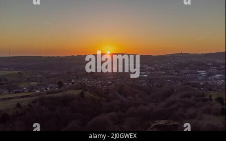 Luftaufnahme zeigt Hartshead Pike, wie die Sonne hinter einem Hügel über dem Dorf Mossley im Großraum Manchester untergeht Stockfoto