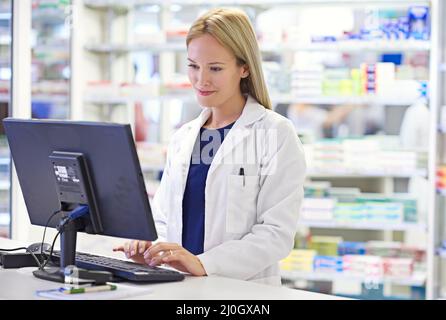 Wir überwachen die Geschichte aller Kunden. Aufnahme eines attraktiven Apothekers am Computer. Stockfoto