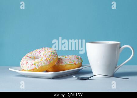 Frühstück für die Liebsten - frisch gebrühter Kaffee in einer Tasse und 2 bunte Donuts Stockfoto