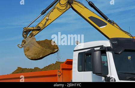 Bagger belädt einen LKW mit Aushub Stockfoto