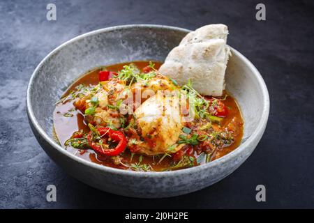 Traditionelle spanische Meeresfrüchte im modernen Stil, zarzuela de Pescado, serviert mit Fisch und Brot in roter Sauce als Nahaufnahme in einem Design-Bogen Stockfoto