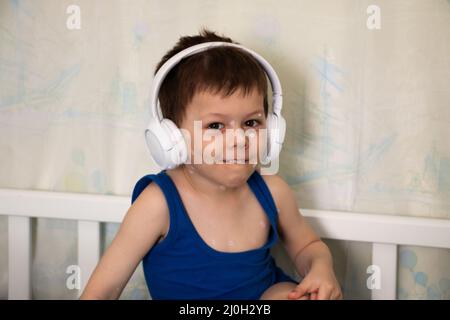 Porträt eines glücklichen lächelnden Kindes mit Windpocken, die Ohrhörer tragen. Kleinkind mit roten juckenden Pickel am ganzen Körper hört Musik oder Hörspiel Stockfoto