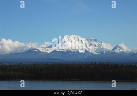 Eine wunderschöne Alaska-Wildnis-Landschaft mit schneebedeckten Bergen, umhüllt von Wolken mit dichten Wäldern und einem schönen See im Foregrou Stockfoto