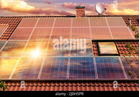 Fotocollage von Solarzellen, Photovoltaik auf dem roten Dach eines Hauses und einem schönen Himmel mit untergehenden Sonne. Alternative Stromversorgung. Konz Stockfoto