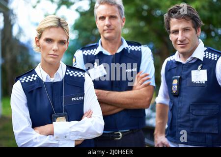 Die Offiziere sind dabei. Kurzer Schuss von drei ernsthaften Mitgliedern der Polizei. Stockfoto