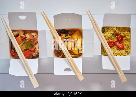 Drei Take Away Papierschachteln mit asiatischen Lebensmitteln in Reihe auf weiß gelegt gefüllt Stockfoto