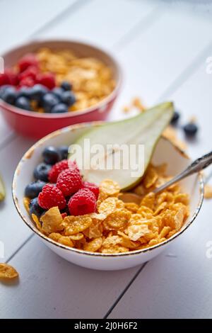 Golden Cornflakes mit frischen Früchte Himbeeren, Heidelbeeren und Birne in Keramik Schüssel Stockfoto