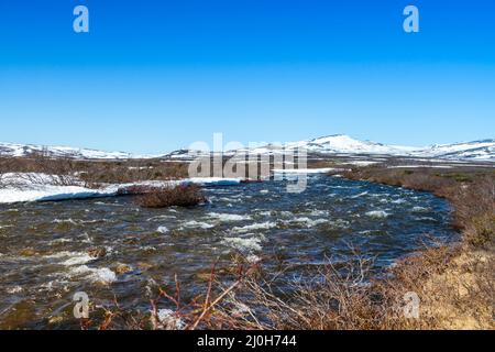 Frühlingslandschaft im Dovrefjell, Norwegen, mit Bach, Felsen, Hügeln, Berge und Schneeflecken Stockfoto