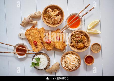 Frittiertes knuspriges Hähnchen in Semmelbröseln auf weißem Holztisch mit Salat und Gewürzen Stockfoto